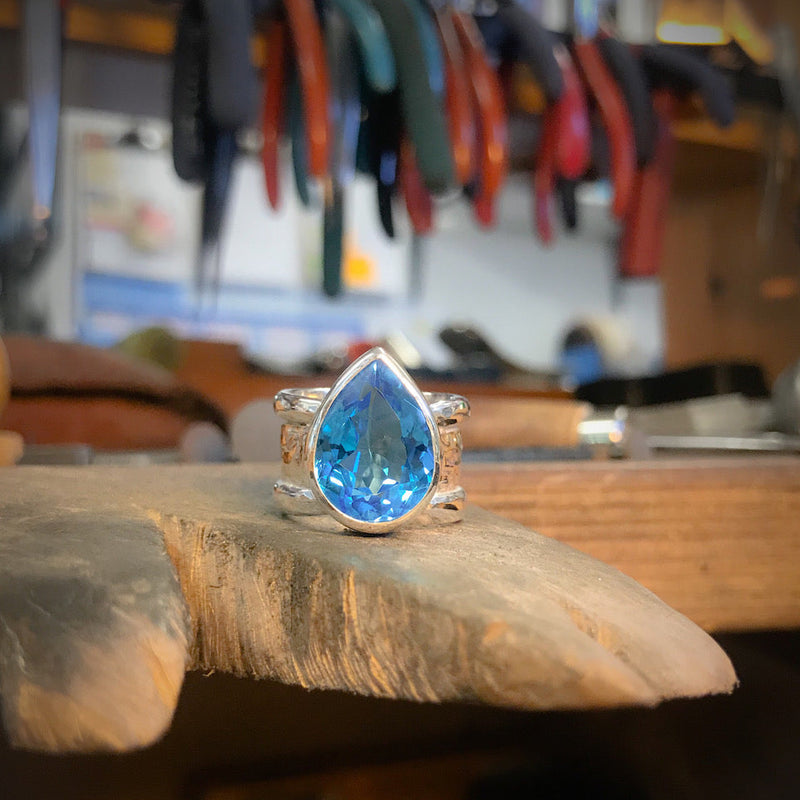 Teardrop-shaped blue gemstone ring on a wooden surface with tools in the background